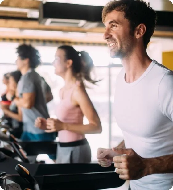 Grupa zaposlenih trči na trakama u svetlom korporativnom fitnes centru, nasmejani i usredsređeni tokom treninga.