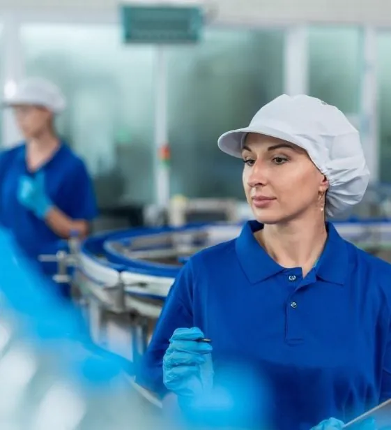 Žena u plavoj uniformi i mrežici za kosu pregleda flaširanu vodu na proizvodnoj liniji u fabrici.