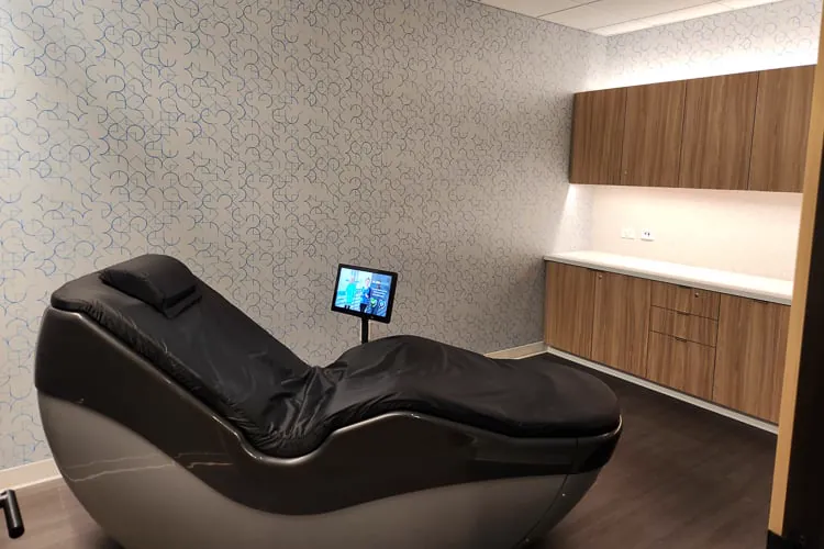 Privatna wellness soba sa crnom masažnom foteljom, ekranom osetljivim na dodir i drvenim ormarićima.