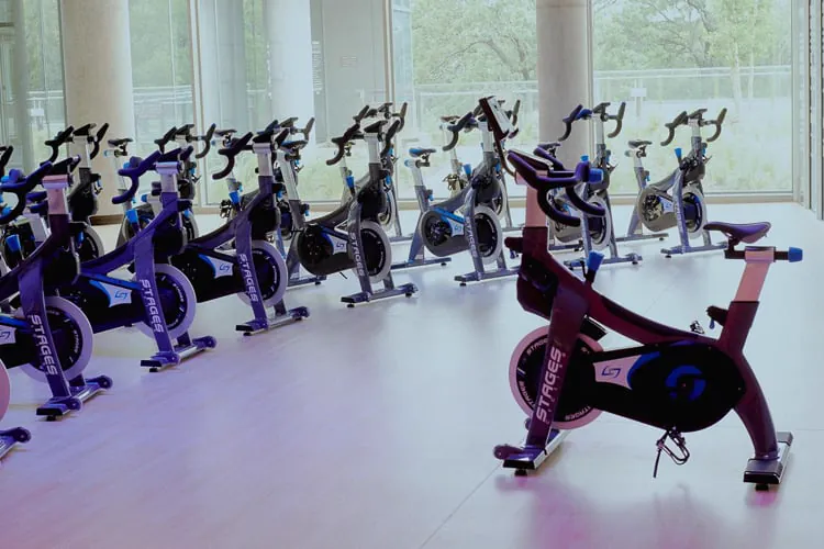 Studio za indoor cycling sa više Stages sobnih bicikala u sunčanoj prostoriji sa prozorima od poda do plafona.