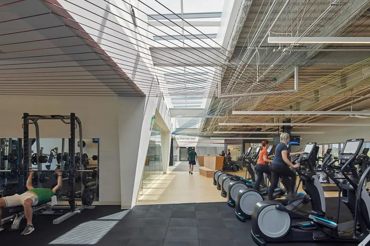 Ljudi koriste kardio opremu i opremu za snagu u prostranom, suncem obasjanom fitnes centru modernog dizajna.