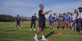 Sportisti USA Football slušaju trenera tokom treninga flag footballa na terenu.